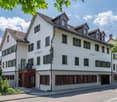 white painted building, multiple windows, brown roofs, balconies on some windows, street entrance with parking