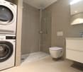 Laundry room with washing machine, dryer, glass enclosed shower area, a toilet, and vanity with sink.