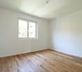 Empty room with white walls, wooden floor, window on the left side