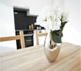Modern dining room with wooden table, white flowers in a silver vase, white cabinets, gas stove and oven in black
