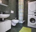green mosaic tiles, white toilet, white sink, built-in shelves, washing machine, dryer, shower curtain, and a green rug