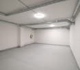 Empty room, white walls, grey floor, several pipes on the ceiling