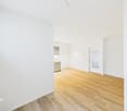 empty room, wooden floor, white walls, window, kitchen area with sink and cabinets