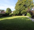 large grass field, trees, shrubs, gravel path, houses at a distance