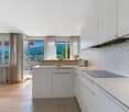 Modern kitchen with white cabinets, gray countertops, and a herringbone tile backsplash. Large windows provide a scenic view of the surrounding mountains and landscape.