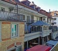 multi-story building, brick facade, multiple balconies, metal railings, windows with white frames, a car parked on the street