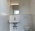 small bathroom with white tiles, white sink, white toilet, mirror