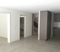 Empty room with white walls, tiled floor, open door, and a small sink in the corner