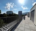 A balcony with a metal railing, tiled floor, and a view of the city and mountains.