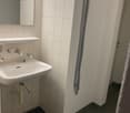 Bathroom with white tiles, white sink, mirror, and black mat