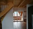 Empty room with wooden ceiling, white walls, wooden staircase, and hexagonal tile flooring. There is a glass door leading to an outdoor area.