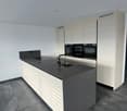 modern kitchen, grey island countertop, black sinks, grey flooring, white cabinets, double oven, white walls