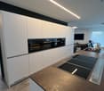 Modern kitchen with white cabinetry, induction stove, double oven, kitchen island, open floor plan
