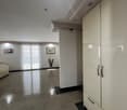 Empty room with white walls, large windows, marble floor, large white wardrobe, picture frames on the wall, and a plant in a vase.