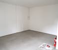 Empty room with white walls and gray tile flooring. There is an electrical panel on the wall.