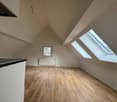 Attic room with slanted ceiling, hardwood flooring, and large skylight windows providing natural light.
