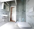 White tiled walls, white sink, white toilet, glass shower enclosure, white towel bar, white light switch plate