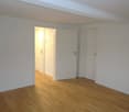 Empty room, wooden floor, white walls, two doors.