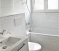 Bathroom with white tiles, modern fixtures, glass shower head, bathtub, toilet, sink with two drawers, large window