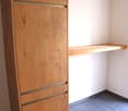 A wooden wardrobe with three drawers and an empty shelf on the wall