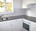 Stainless steel sink, dishwasher, oven, stovetop, tiled walls, white cabinets, window