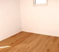 white walls, hardwood floor, power outlet on wall, window with a white frame