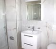 modern bathroom, white marble walls, shower, toilet, white sink, silver faucet, mirror, vanity with drawers