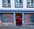 Facade of building with 3 glass windows on the top floor and 2 glass display windows, entrance with a pink interior
