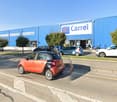 A large blue building with the Carrel logo, surrounded by a parking lot with several cars parked in front of the store.