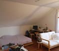 attic room with bed, work desk, white sofa with pillows, floor heater, window, ceiling lamp