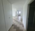 White-painted walls, checkered floor tiles, open doors to another room, tall cabinet