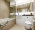 modern bathroom with bathtub, white cabinets, mirrors, shower, sink, and toilet