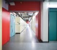 Long and narrow corridor, red and green doors, shiny tiles, closed doors on both sides.