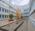 Blue building, multiple windows, landscaped courtyard, wooden pathway, metal poles, plants, benches.