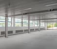 An empty office space with a ceiling featuring recessed lighting, glass windows, central heating radiators, and a glass door leading to the exterior. No visible furniture or personal belongings.