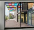 entrance to a building, large windows, glass door, colored glass roof, pavement, plants, greenery