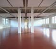 large open space, red floor, white walls, large windows, white pillars, white ceiling panels, white radiators
