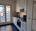 Compact kitchen with white cabinets, black countertops, and a stove. The kitchen has a sliding glass door leading to a balcony or terrace.