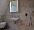 small bathroom with white tiles, toilet, sink, shower, mirror