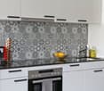Modern kitchen with white cabinets, black and white patterned backsplash, black countertop, built-in oven, and a red coffee machine.