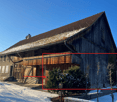 Timber-framed house with tiled roof, wooden balcony, wooden walls, entrance on the left, snow on the roof