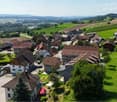 several houses in a village surrounded by green hills and farm fields