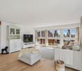 Living room with white walls, wooden floor, large windows, white furniture, TV, rug, and decorative items