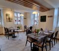 A restaurant with wooden ceiling, white walls, tiled floor, tables and chairs, radiators, and paintings on the wall.