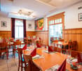 Wooden walls, wooden tables and chairs, multiple chandeliers, picture frames on the wall, red napkins on the table