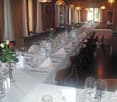 Dining room with long table, chairs, white tablecloth, wine glasses, flowers, napkins, cutlery, lamps
