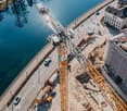 Aerial view of construction site with cranes and buildings under construction by a river