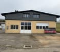 two-story house, yellow exterior, black roof, two glass double doors, several windows, signboard, large parking area
