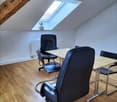 Attic office space with wooden beams, skylight, leather office chairs, and a wooden table
