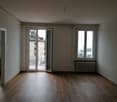 spacious room, wooden floor, two glass doors to a balcony, windows with white frames, radiators